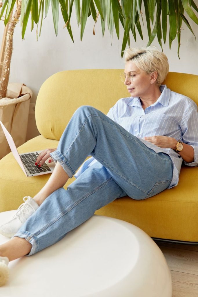 Woman with short blonde hair using laptop while relaxing on a sofa.